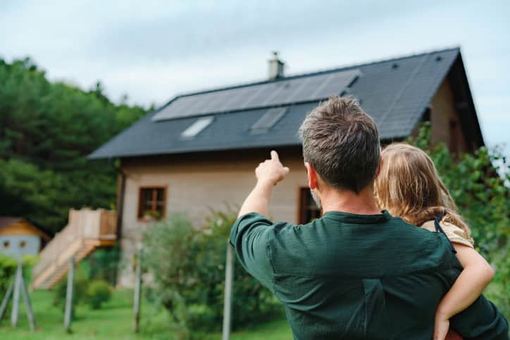 man holding child in arms and pointing at their house